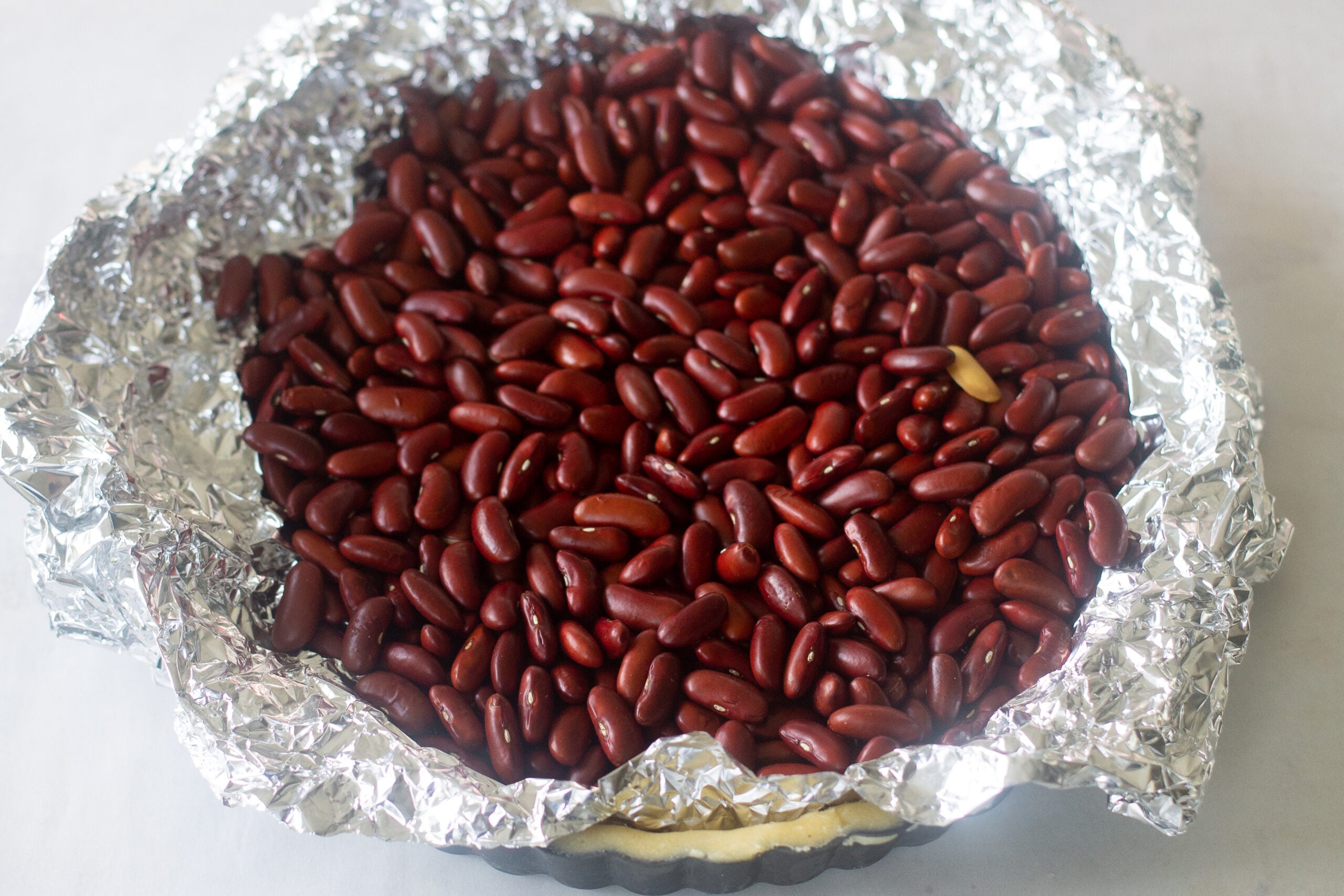 Pastry crust in tart pan lined with foil and filled with dried red beans.