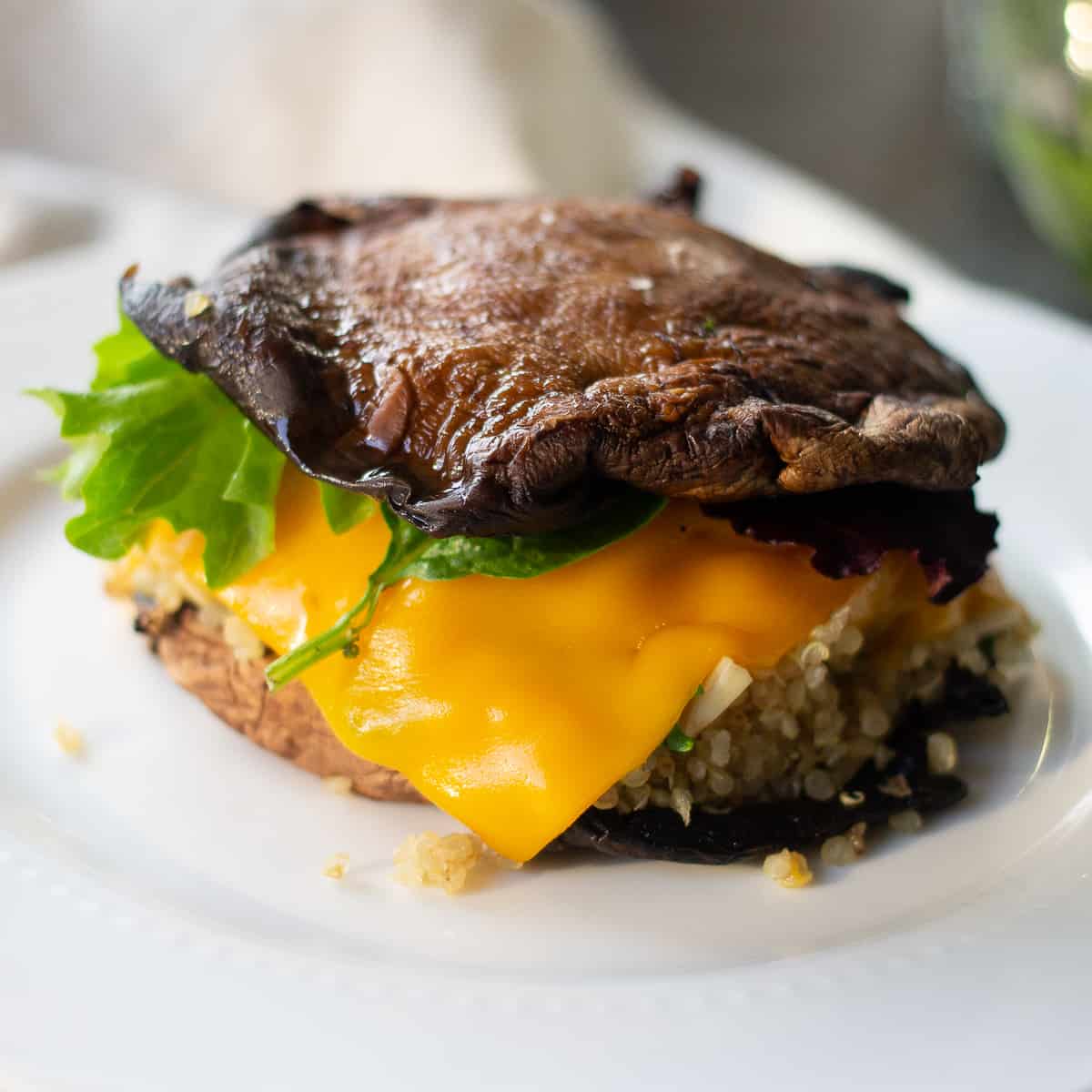 Two roasted portobello mushrooms sandwiching cooked quinoa like a burger with melting cheddar cheese.