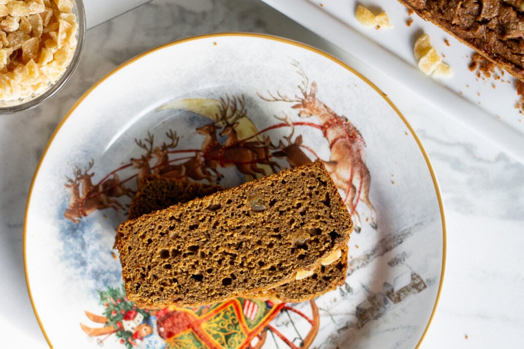 Gluten-free gingerbread loaf slices on Christmas plate with candied ginger on the side.