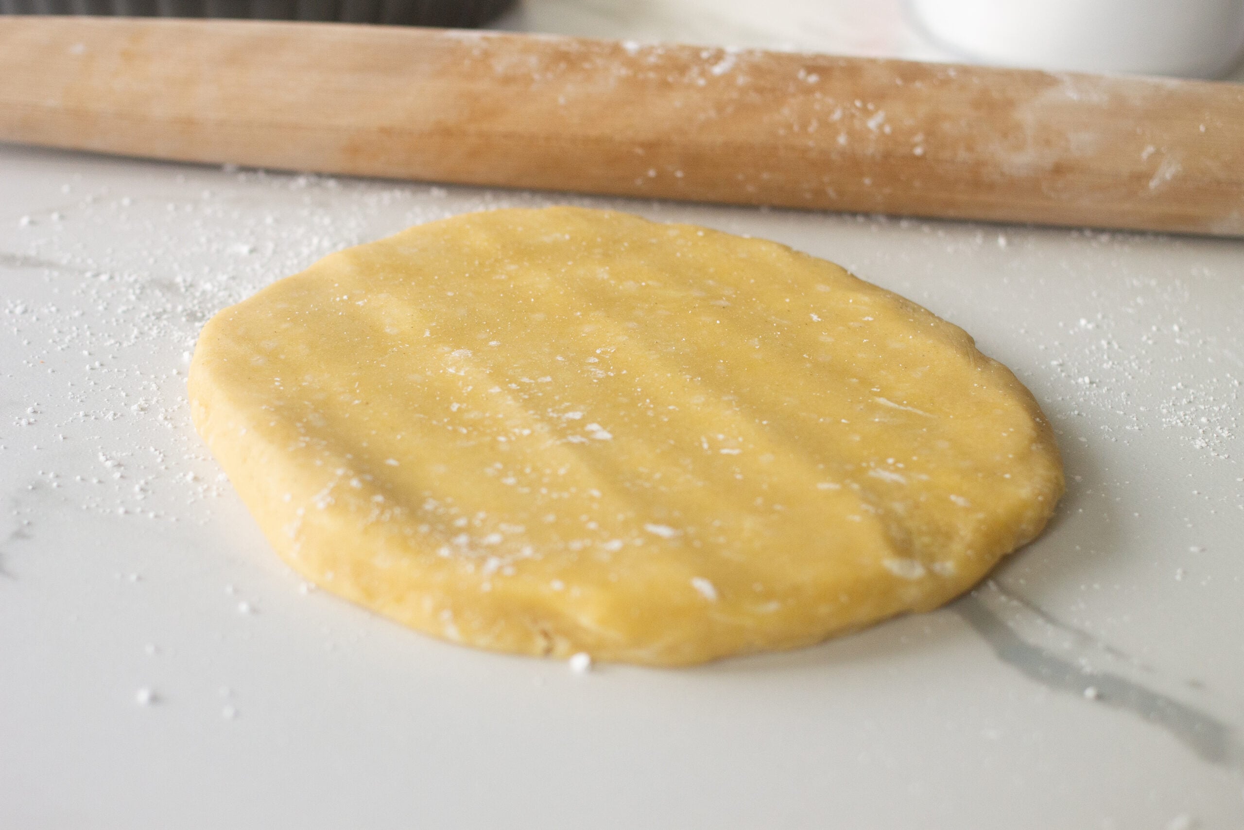 Round disc of pastry dough next to rolling pin on counter.