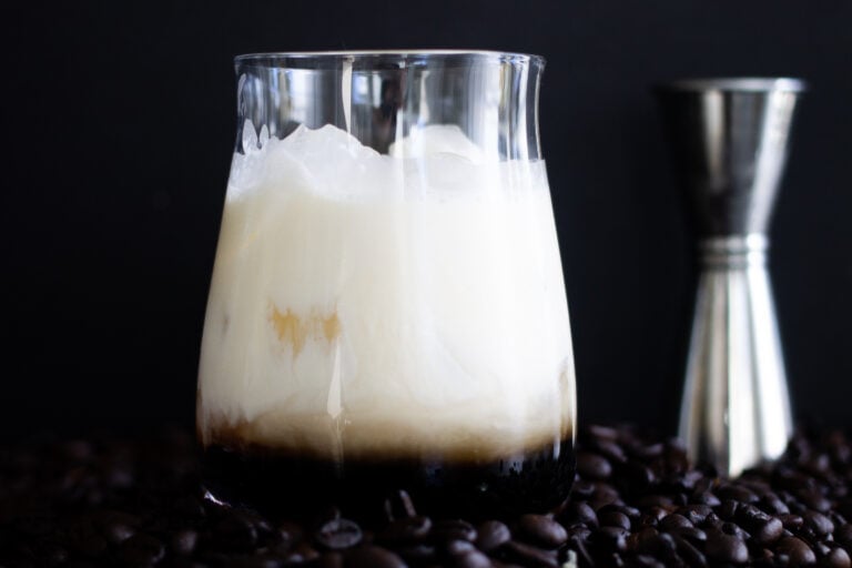 A White Russian cocktail sitting on coffee beans, the most popular of all the Kahlúa drinks.