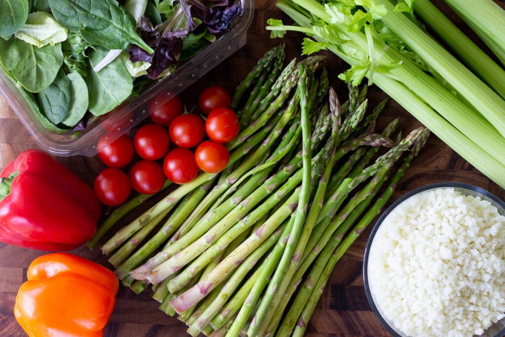 Asparagus, cherry tomatoes, salad greens, celery, cauliflower rice and bell peppers on cutting board.