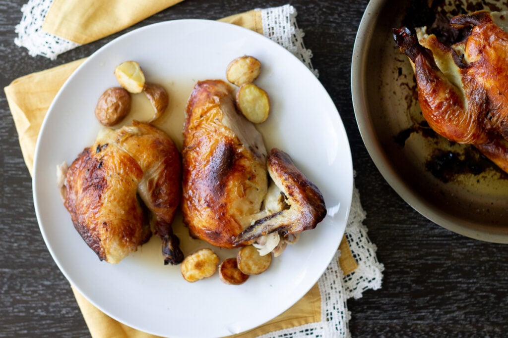 Roasted chicken carved on a plate with small roasted potatoes.