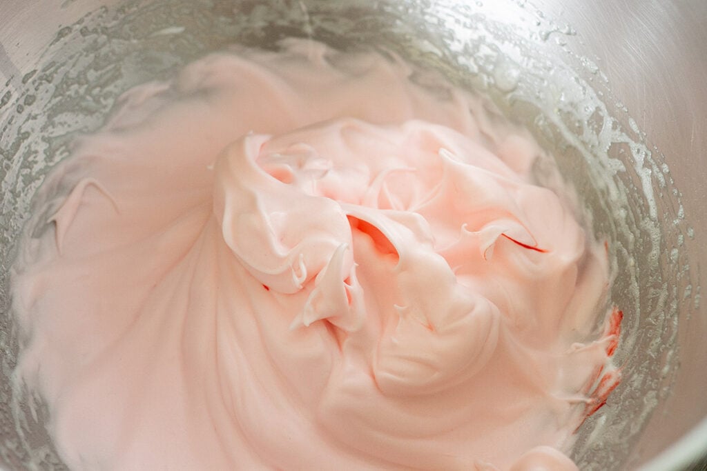 Whipped pink meringue for strawberry french macarons in a stainless steel bowl.