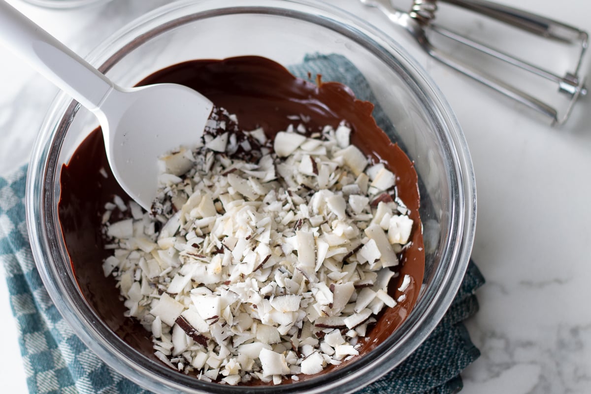 Chopped flaked coconut sitting on top of melted chocolate in a glass bowl.