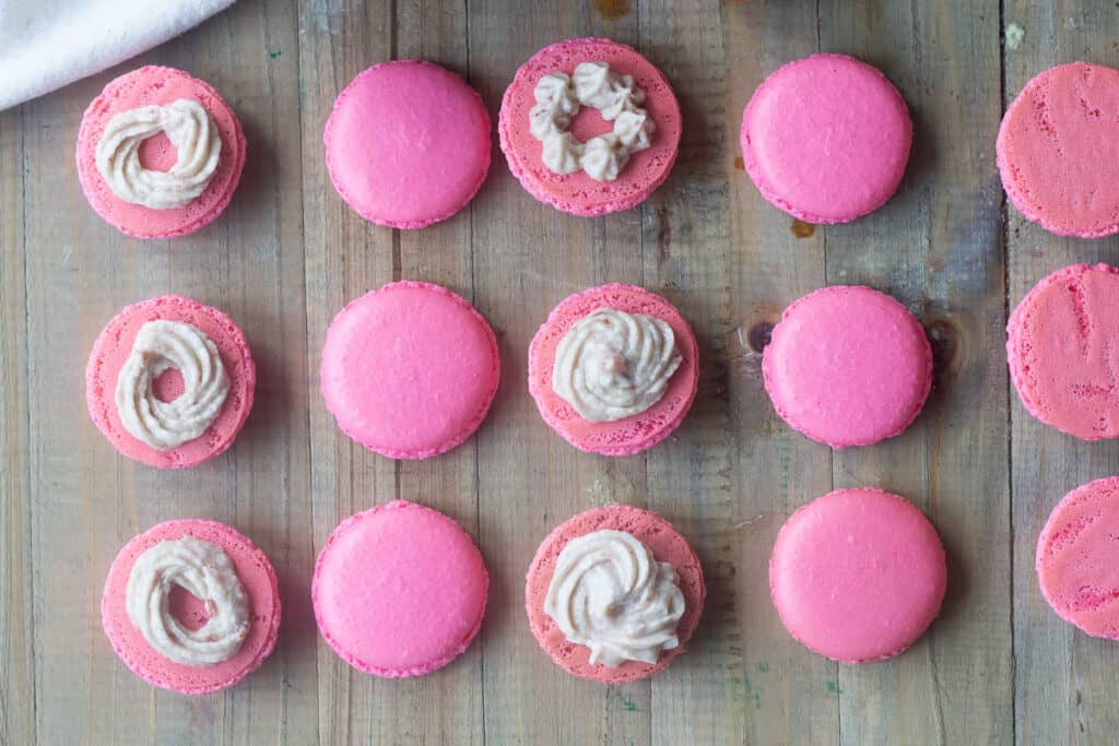 Rows of pink macaron shells alternating upside down and right-side up, with buttercream piped on the upside-down rows.