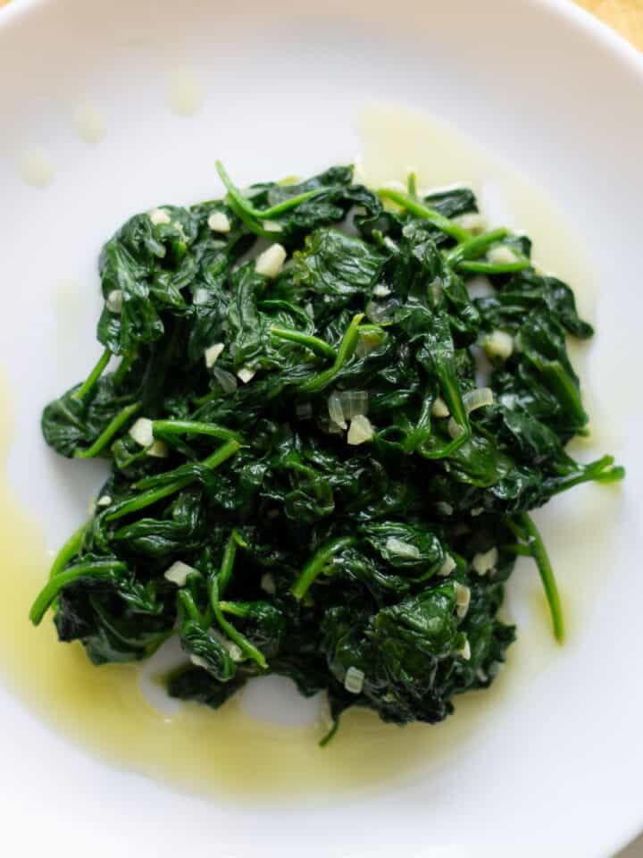 Sautéed spinach on a small white place with a drizzle of olive oil around the rim.