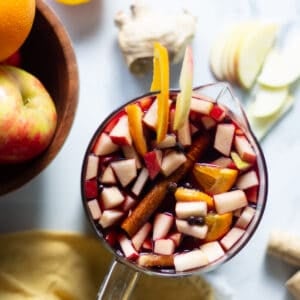A pitcher of apple cider sangria with chopped apples and oranges and whole spices.