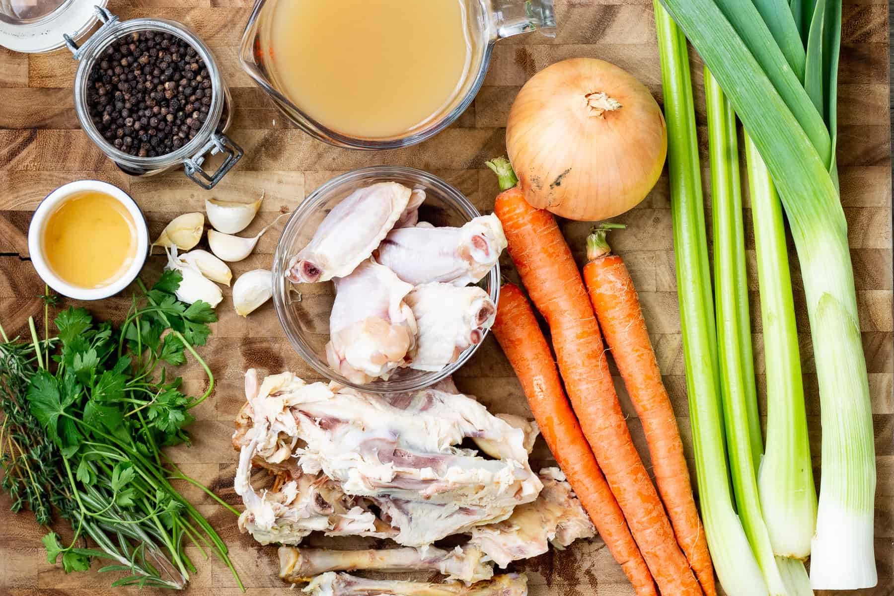 A variety of raw vegetables and herbs for chicken jus on a cutting board.