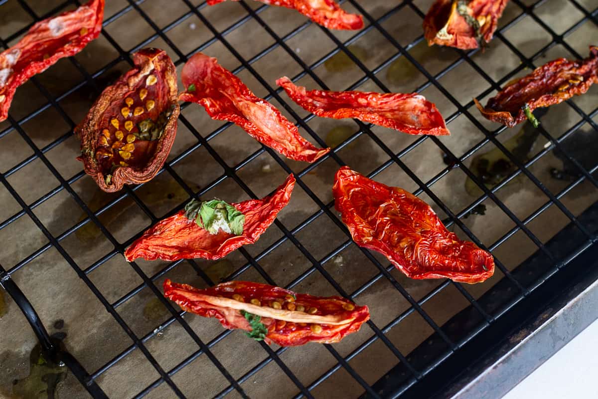 Sun-dreid tomatoes on a rack on a baking pan that just came out of the oven.