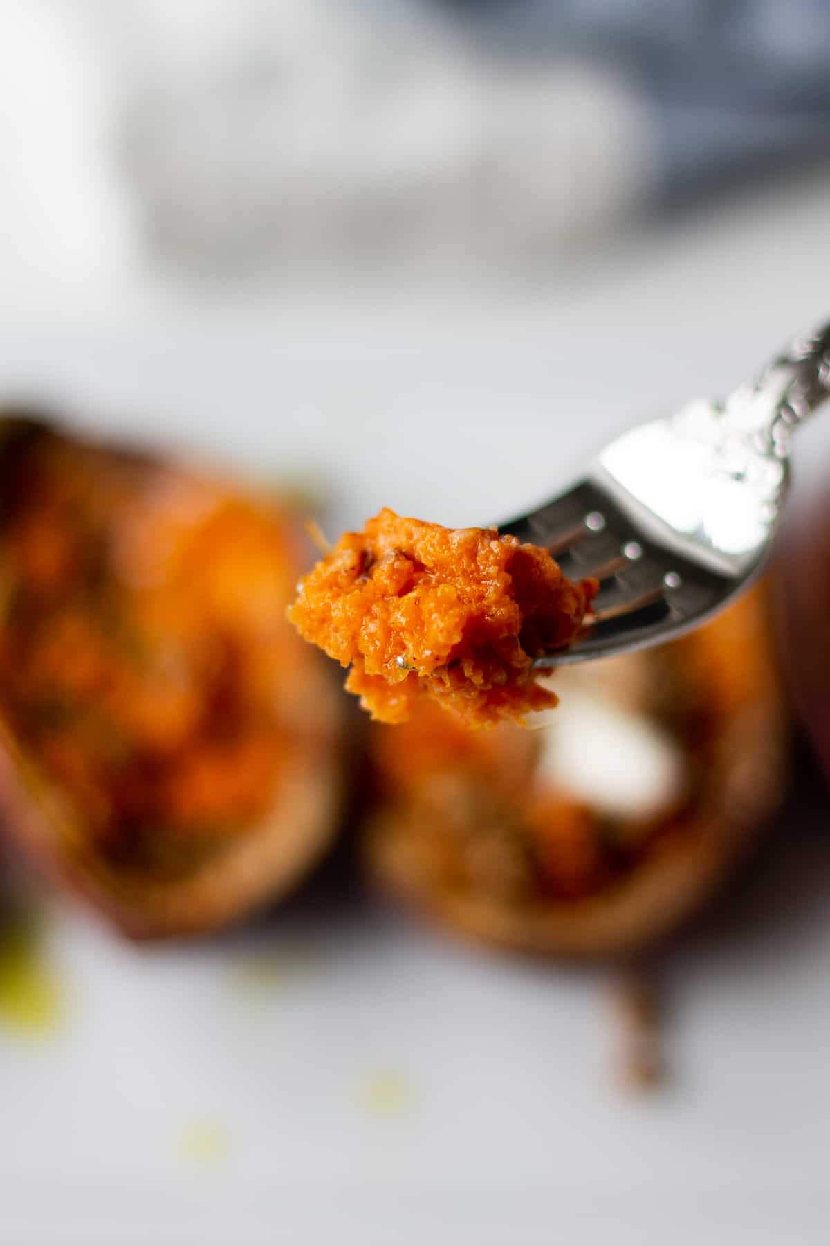 A bite of soft air fryer sweet potato on a fork over the rest of the potato on a plate.
