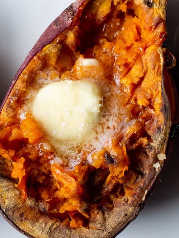 Close up view of a sweet potato half with butter melting on top in the middle of the flesh.