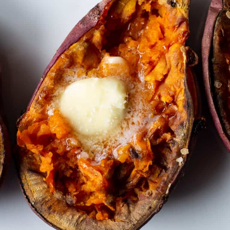 Close up view of a sweet potato half with butter melting on top in the middle of the flesh.