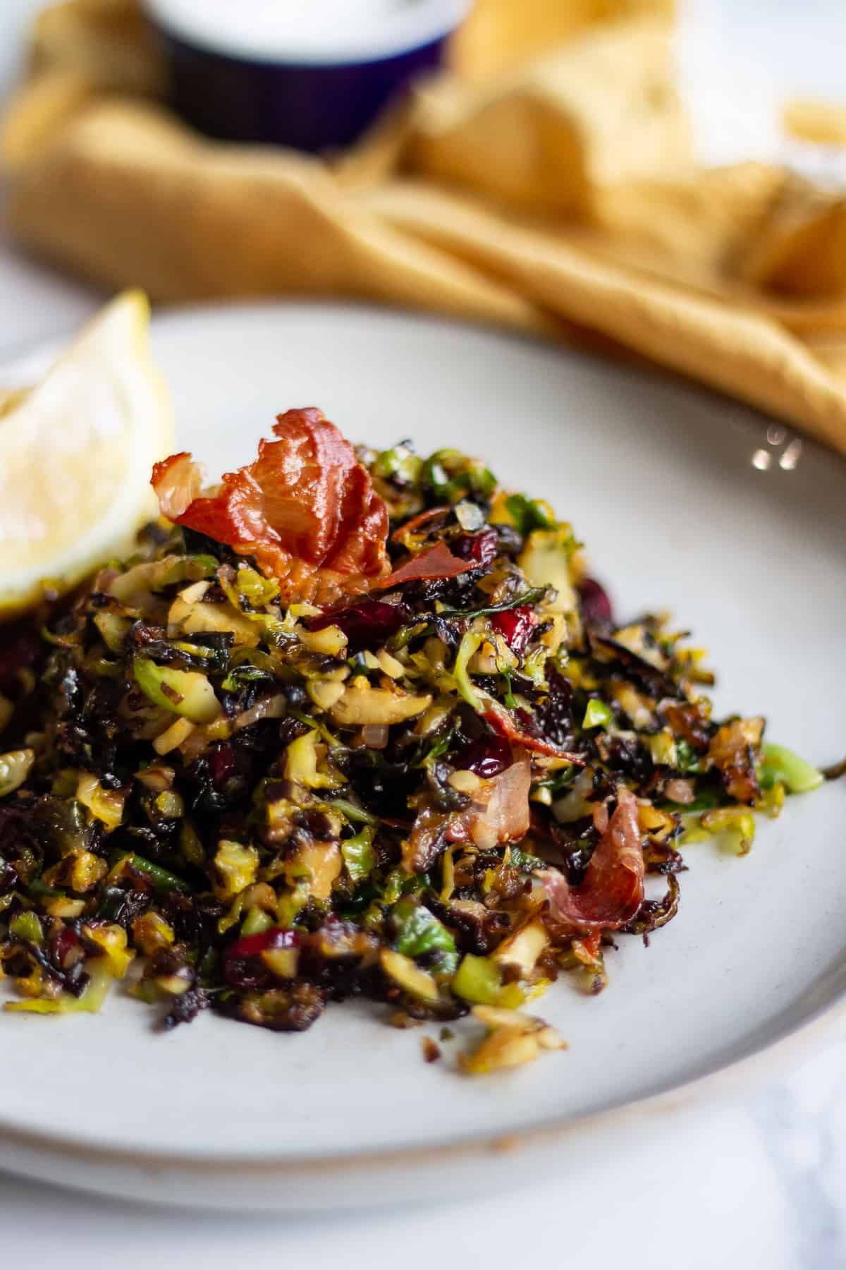 A pile of shredded, sautéed Brussels sprouts on a plate topped with crispy proscuitto.