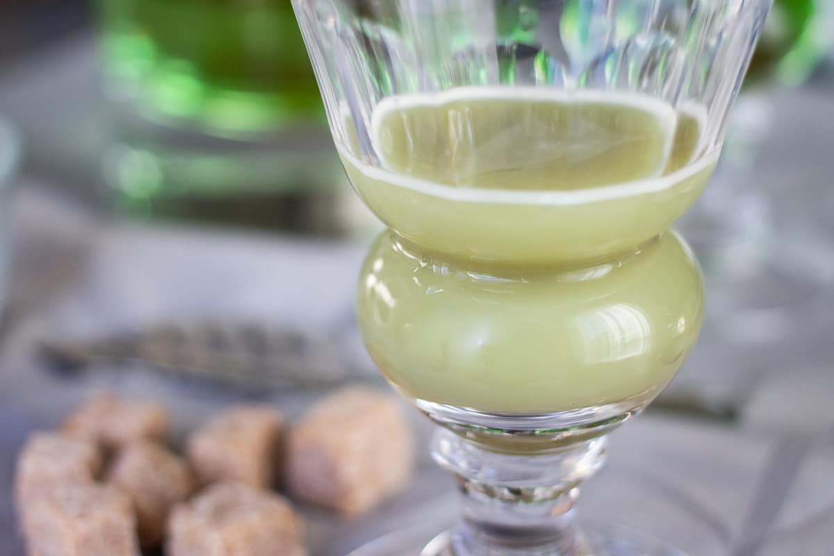 An absinthe glass with a finished drink in it, that is a cloudy, milky green color.