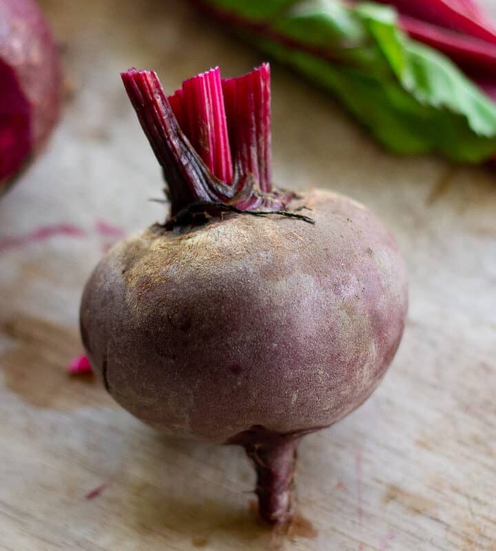 A single red beet on a cutting board with the greens and tap root removed.