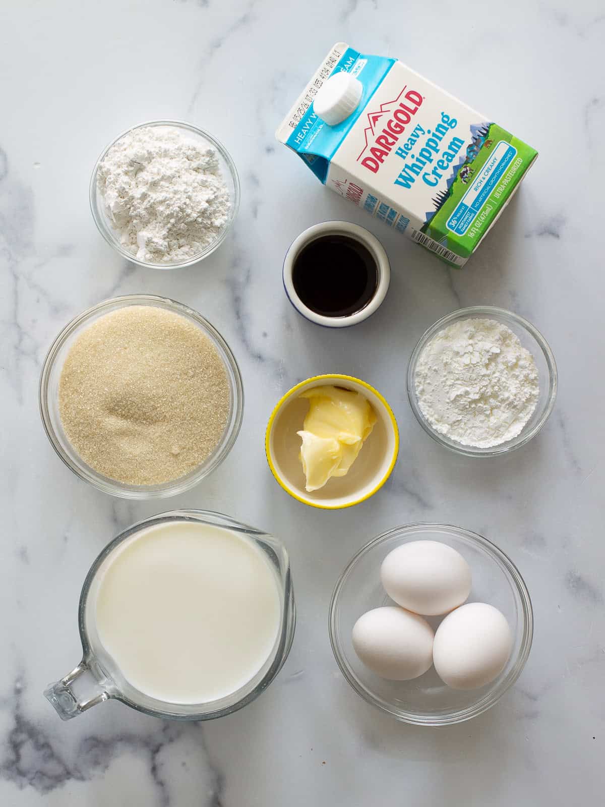 The ingredients for pastry cream on a counter: milk, eggs, sugar, cornstarch, and heavy cream.