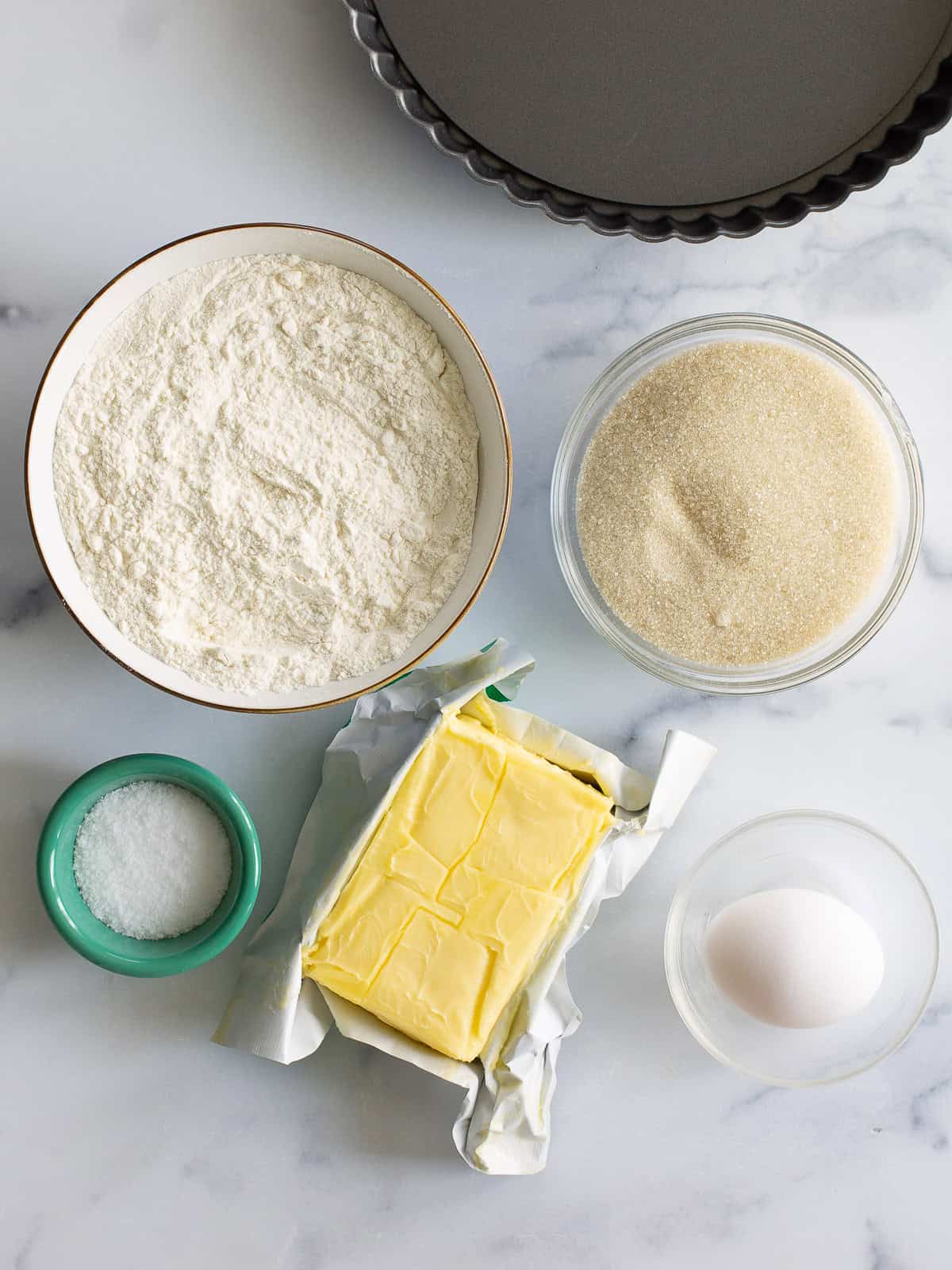 The ingredients for a fruit tart shell on the counter: butter, flour, sugar, an egg, and salt.