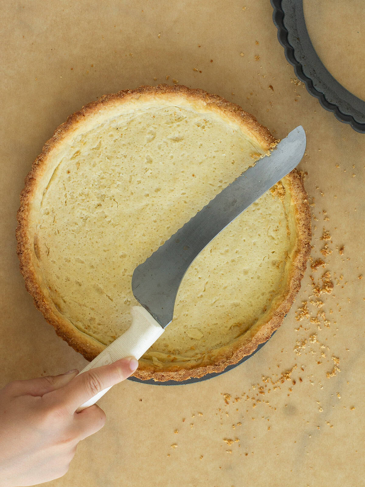 A serated knife lightly chipping away darker edges of a baked tart shell.