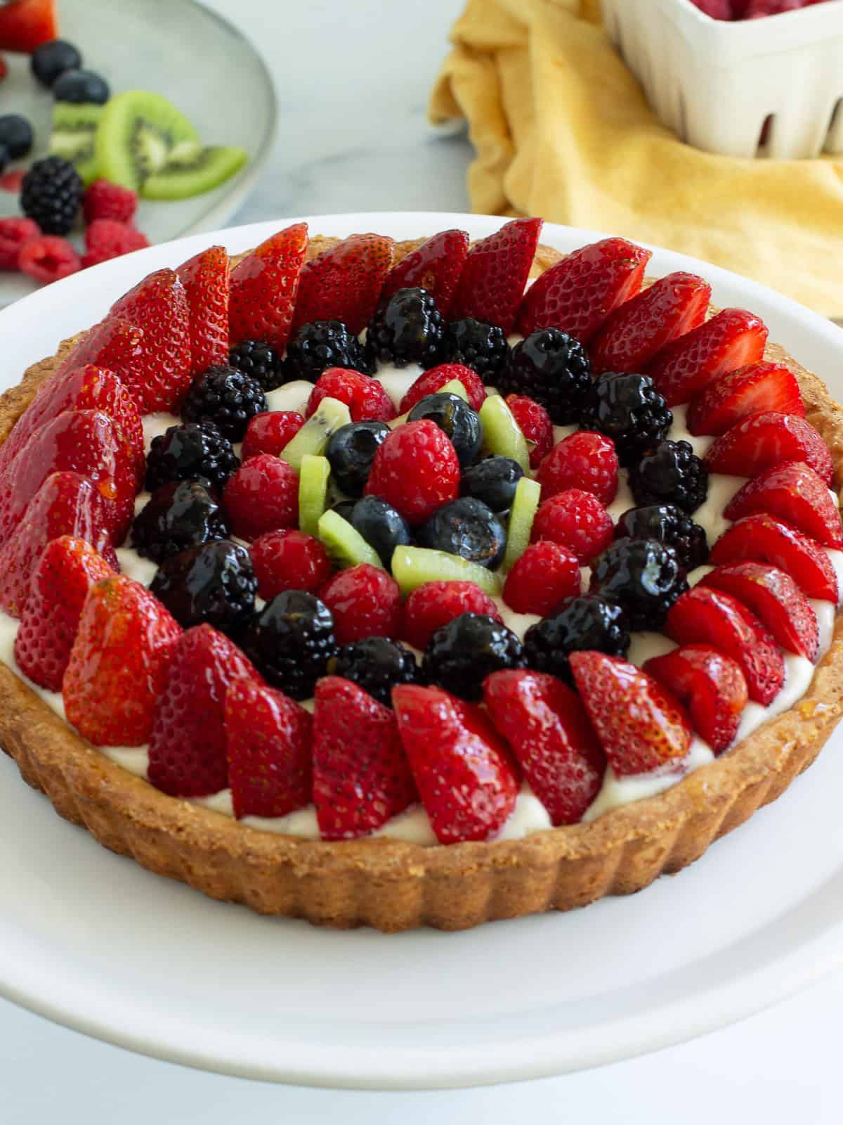 A 45-degree angle view of a classic fresh fruit tart with berries and vanilla pastry cream.