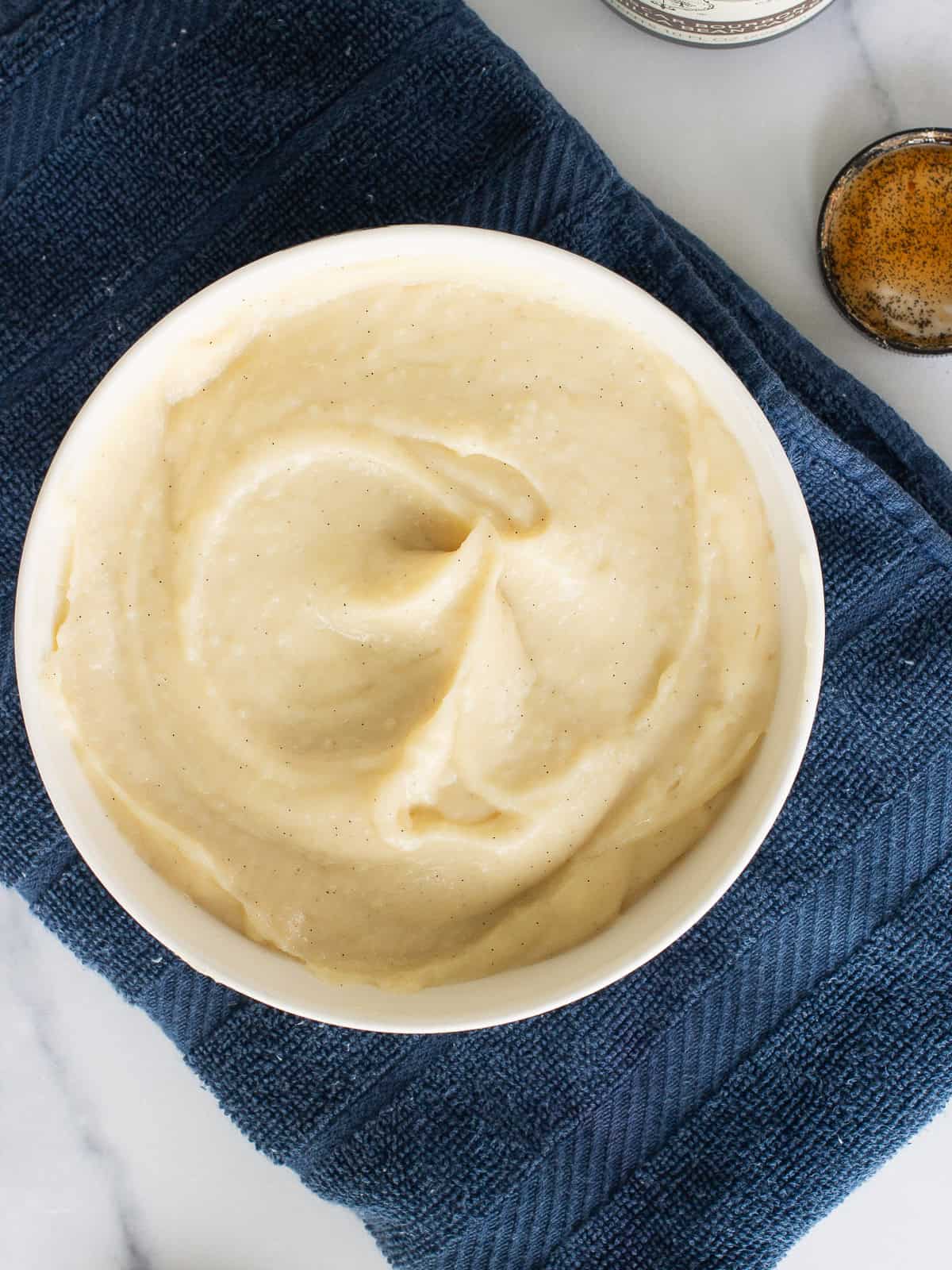 Vanilla bean pastry cream for a fruit tart in a white bowl sitting on a blue towel.