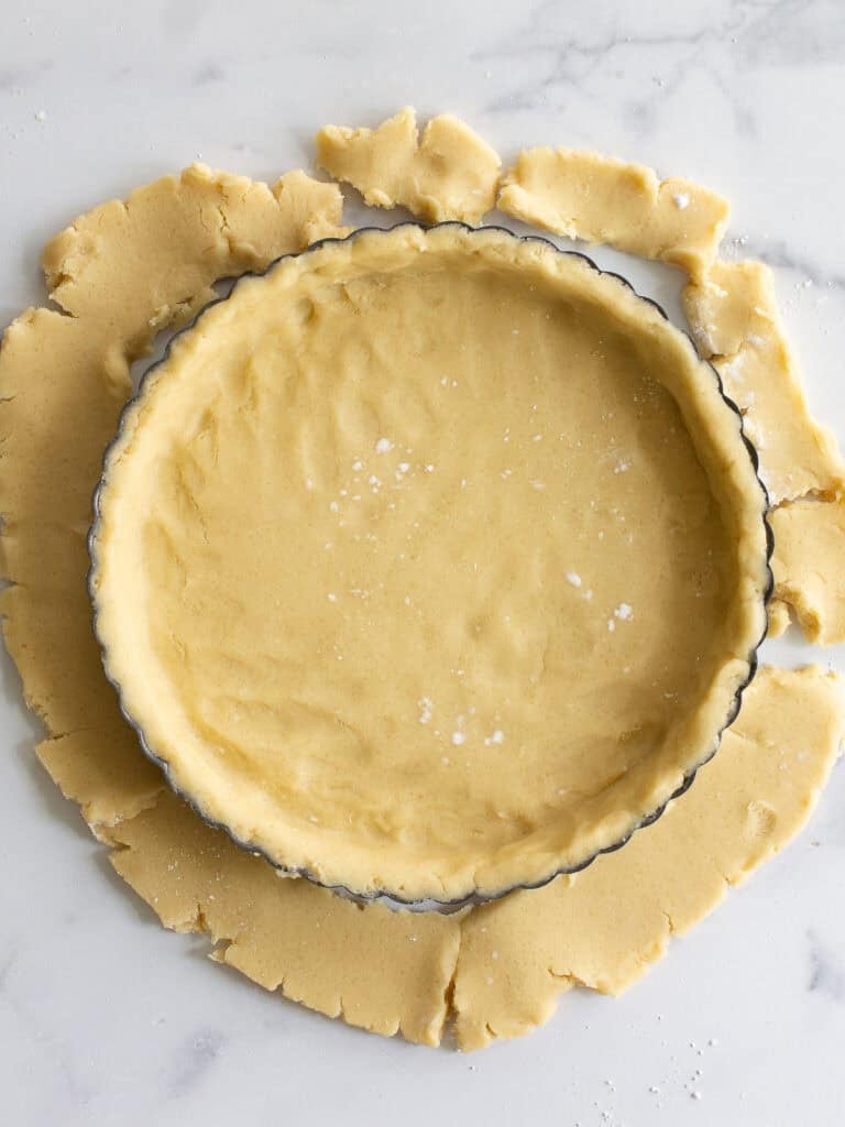 Raw pastry dough pressed into a tart pan with the excess fallen around the edges.
