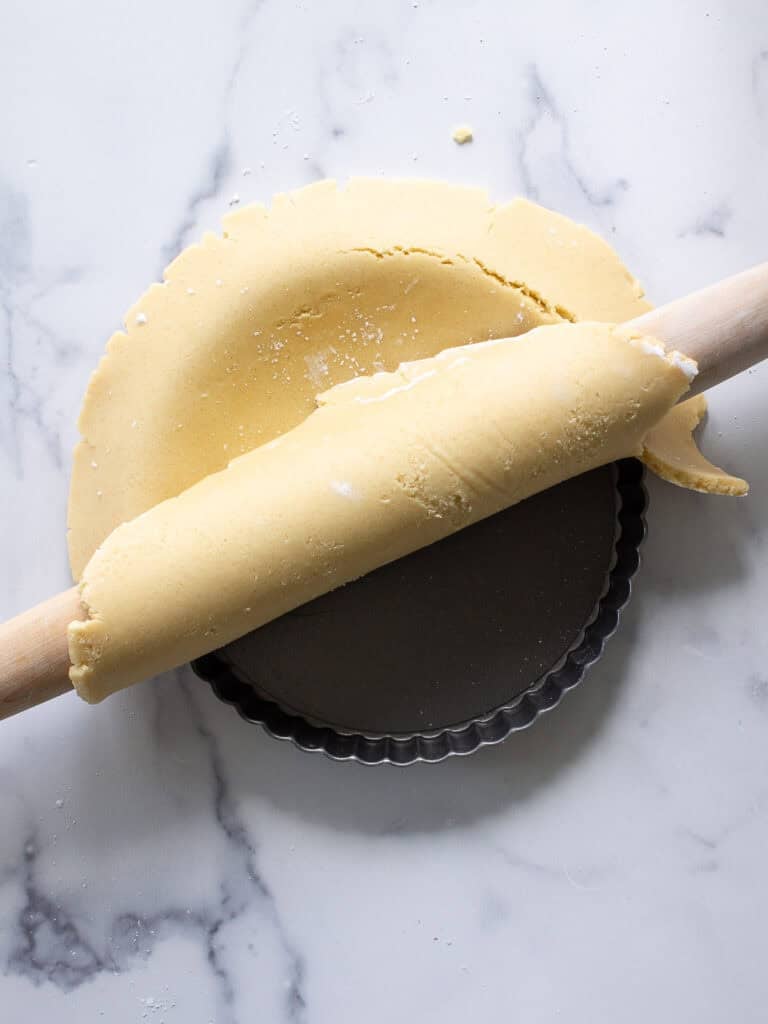 Pastry dough draped over a rolling pin being transfered to a tart pan.