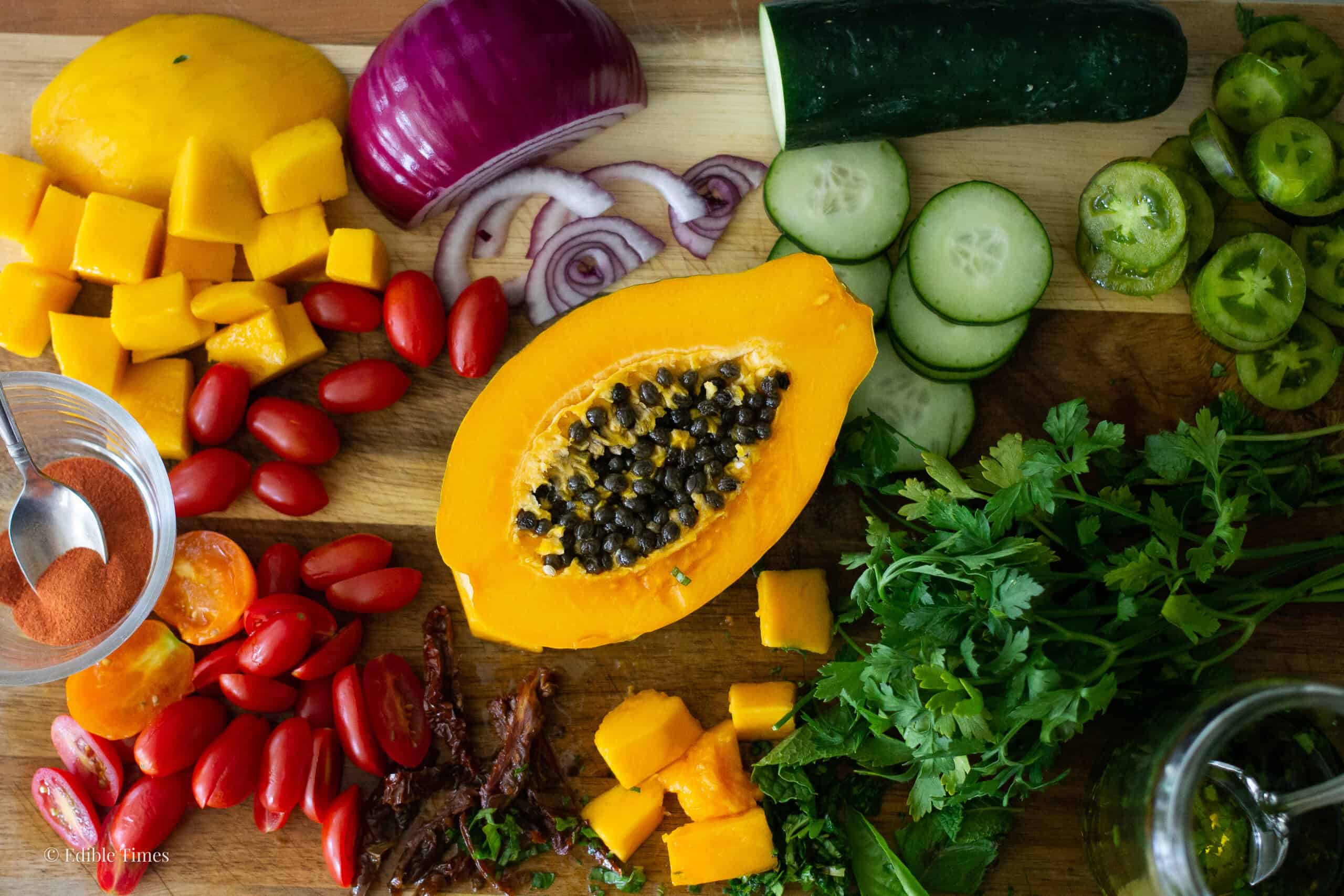 A rainbow of fruits and vegetables on a cutting board with a halved papaya in center.