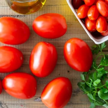 A variety of tomato types on a cutting board with herbs as anti-inflammatory ingredients.
