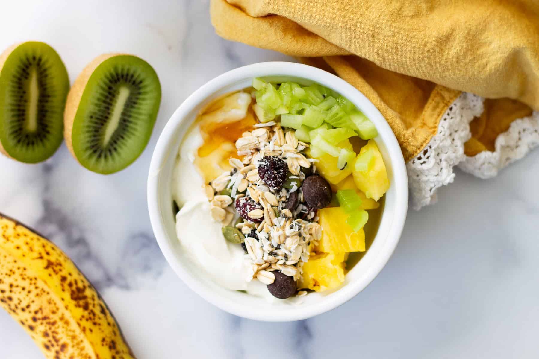 A ramekin of plain yogurt topped with muesli and pineapple and a little honey.